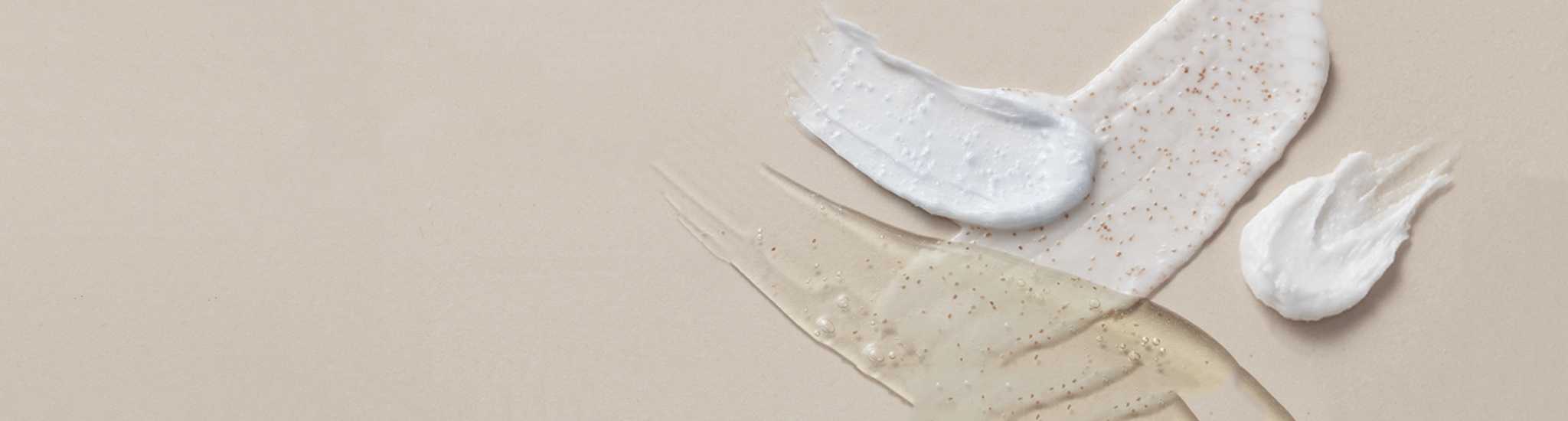 Various skincare product textures are spread on a neutral beige surface, including creamy white, blue, and translucent gels with different consistencies and speckled particles.