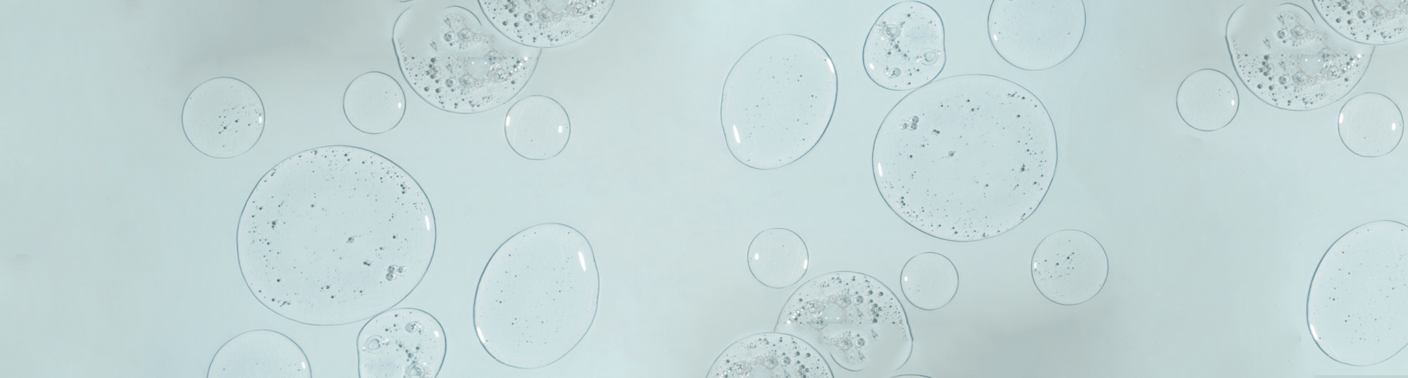 Clear bubbles of various sizes float against a pale blue background, resembling water or soap bubbles. Some bubbles contain small air pockets, giving a textured appearance