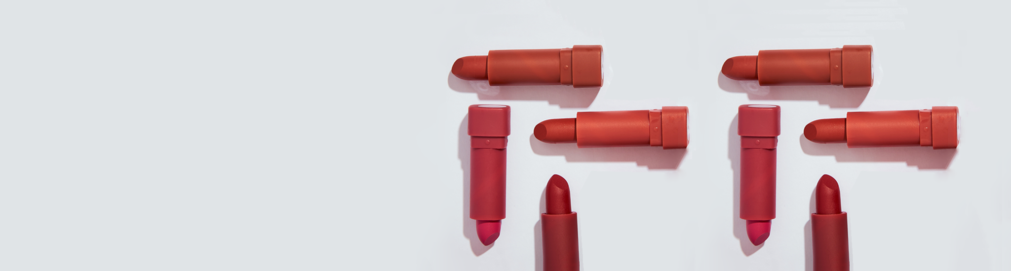 An array of red lipsticks with varying shades, caps off placed on white background casting a shadow.