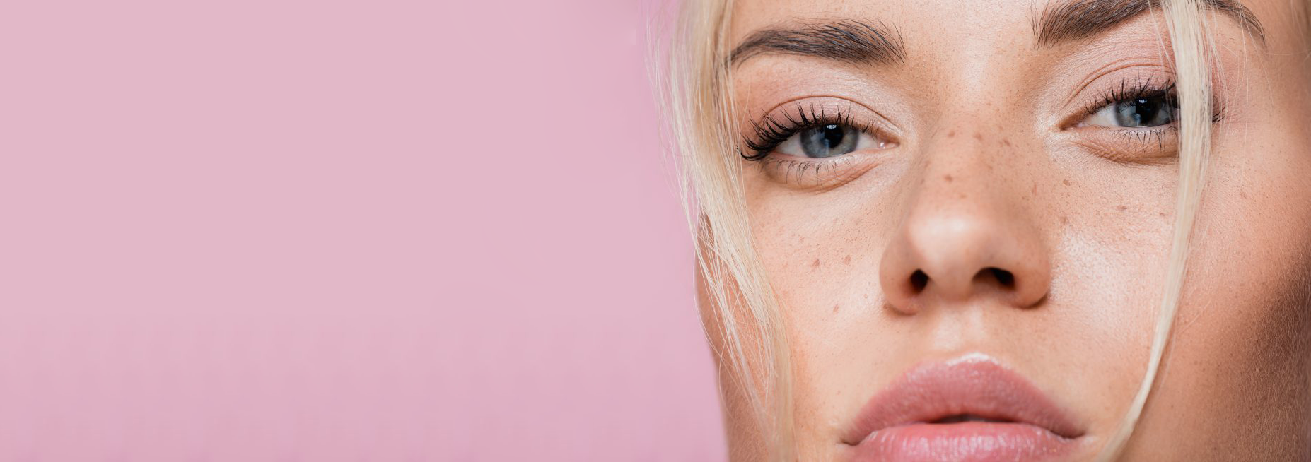 A close-up and partial view of a person's face with blonde hair against a pink background.