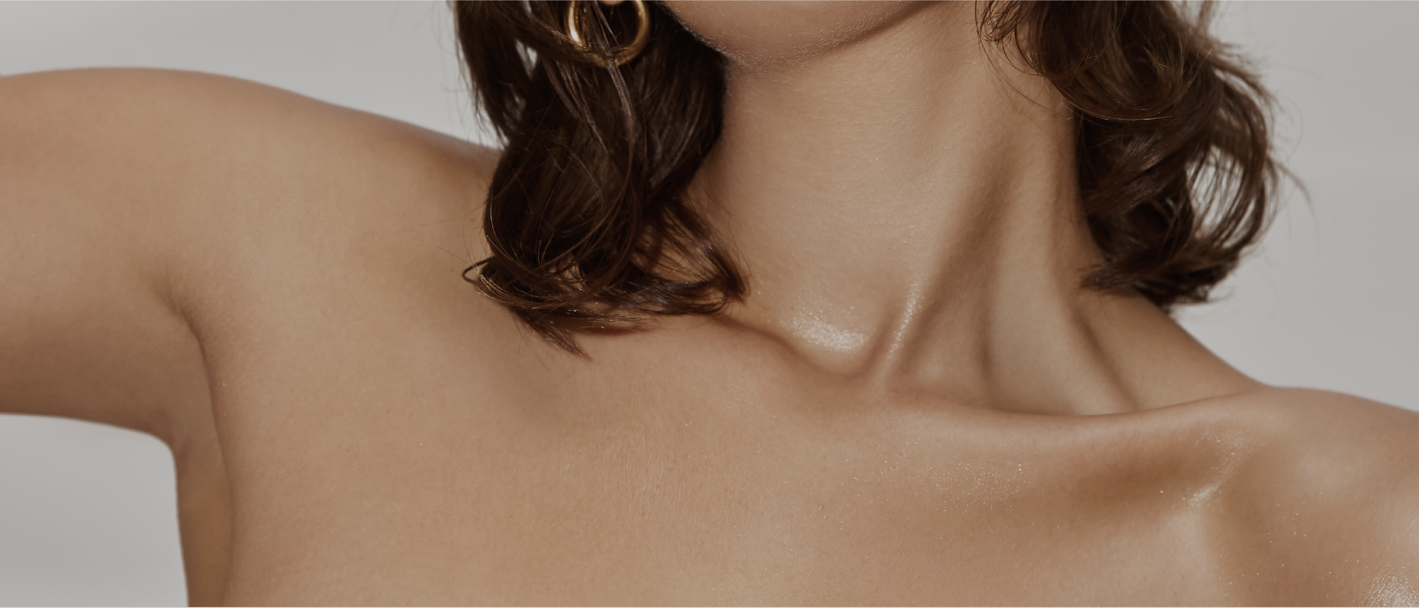 Close-up of the clavicle and shoulders with sunkissed, moisturised skin and brunette hair falling on shoulders. 