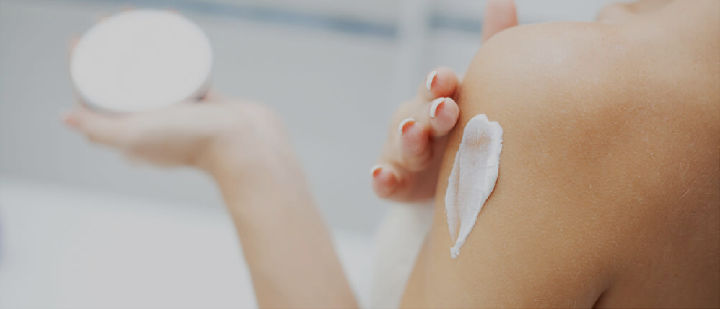 Close-up of a person applying white body cream on their shoulder from a jar.