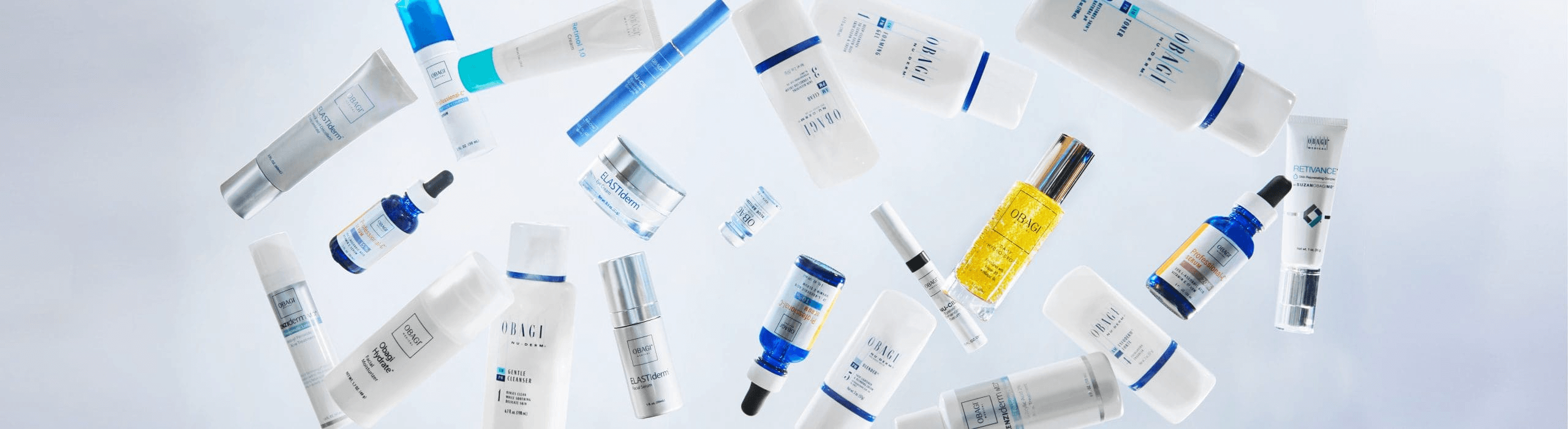 A variety of skincare product bottles and tubes in white and blue hues from Obagi are scattered across a light blue background. The containers are of different shapes and sizes, including droppers, pumps, and tubes.